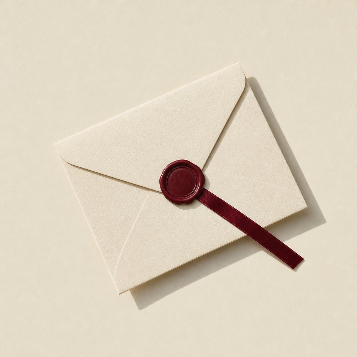 A cream envelope closed with a maroon wax seal and ribbon, centred on cream paper