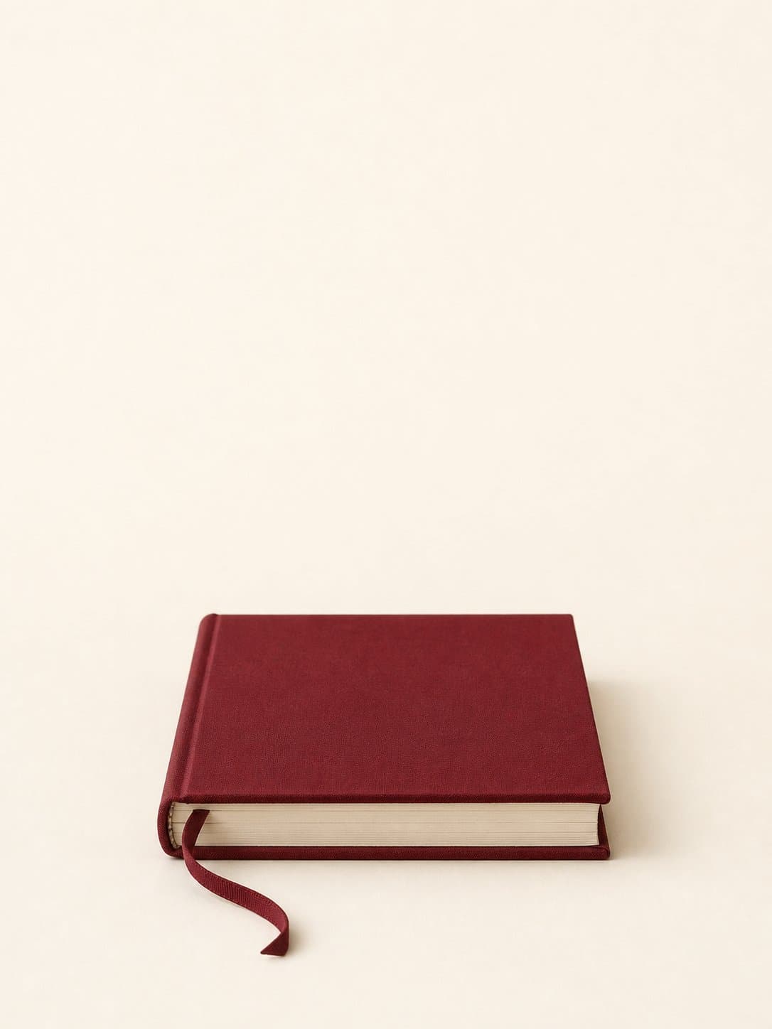 A bound maroon notebook with ribbon, centred on cream paper